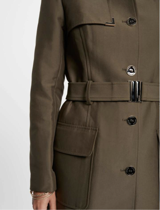 trenchcoat groen klassiek model, Deze super leuke trenchcoat valt mooi ruim over de knieën maar wel met een pittige snit....strak silhouet met een mooie afwerking op de schouders van kleine zilveren ringetjes welke door de stof zijn geponst, leuke gespen op de mouwen voor net even wat meer allure. Deze trenchcoat heeft door het gebruik van een mooie luxe stof (katoen/strech) met een lichte subtiele glans een hele luxueuze look! Dit is wat we noemen een door draag model, voor nu in de herfst helemaal leuk maar ook in het naseizoen en in de killere herfstdagen goed te combineren met een lekker dikke coltrui eronder. Morgan de toi is een frans label, dit betekend alles net even iets strakker.Dit model valt strak op de schouders om de mooie pittige lijn te krijgen, maar mocht je wat meer ruimte willen dan 1 maatje groter bestellen.